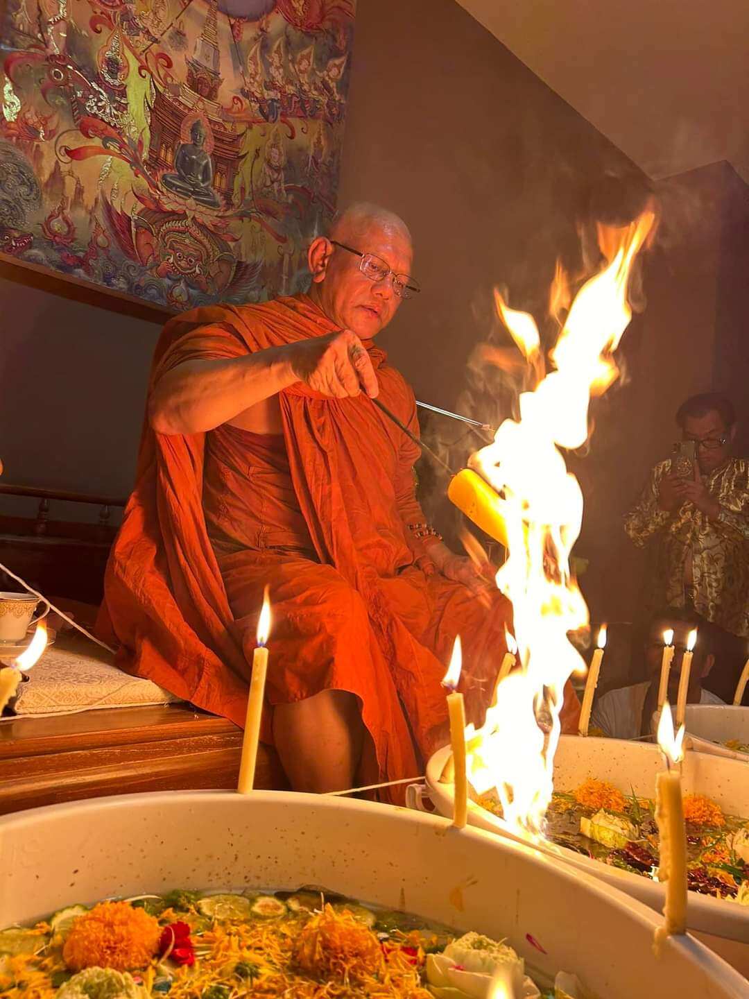 Thai monk blessing Jin-Da-Mani magical bead amulet during a ceremonial fire ritual with candles and offering bowls