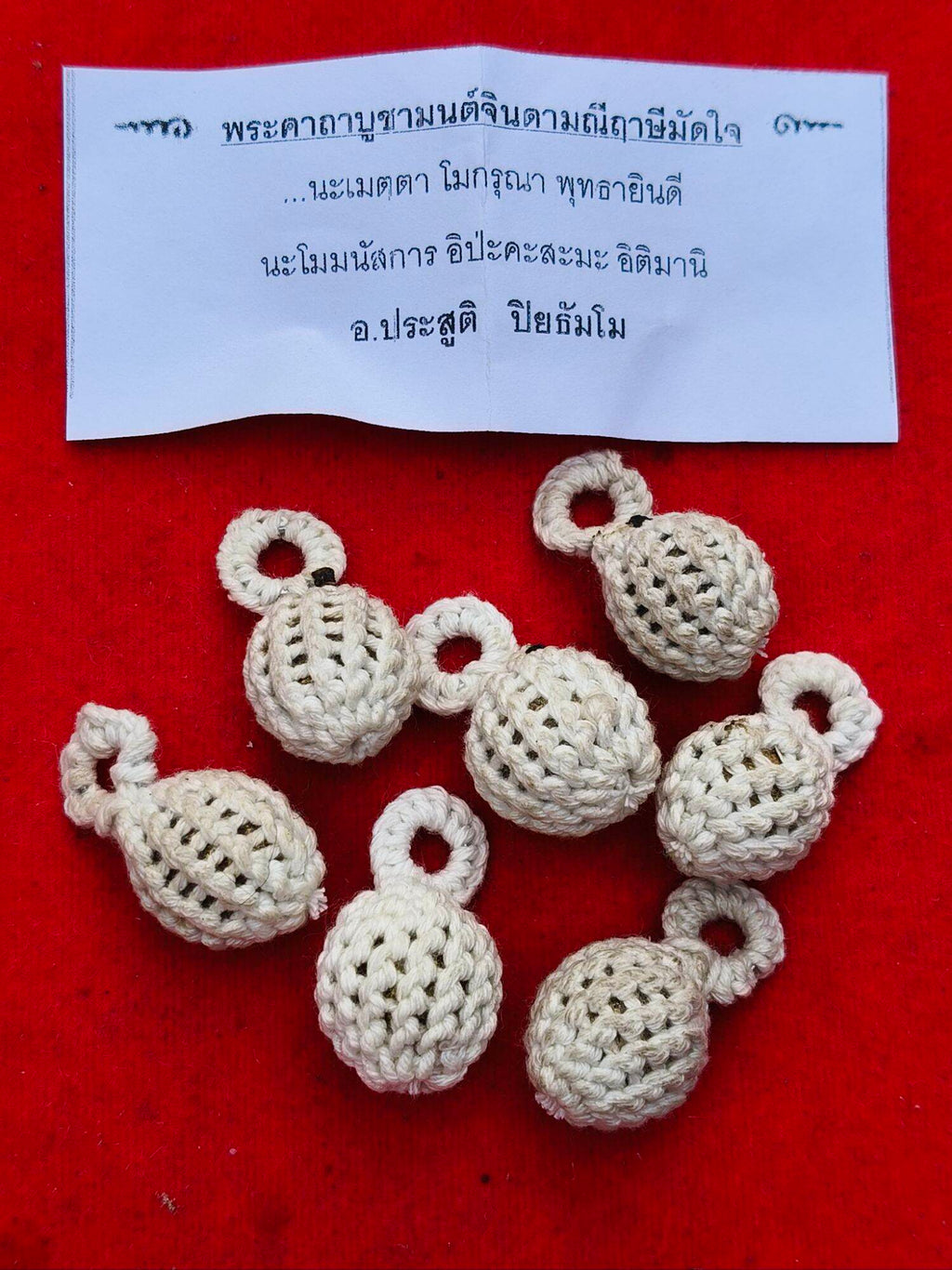 Crocheted ivory bead pendants with loop tops on red cloth and prayer slip Thai Blessing Co Jin-Da-Mani magical bead amulet