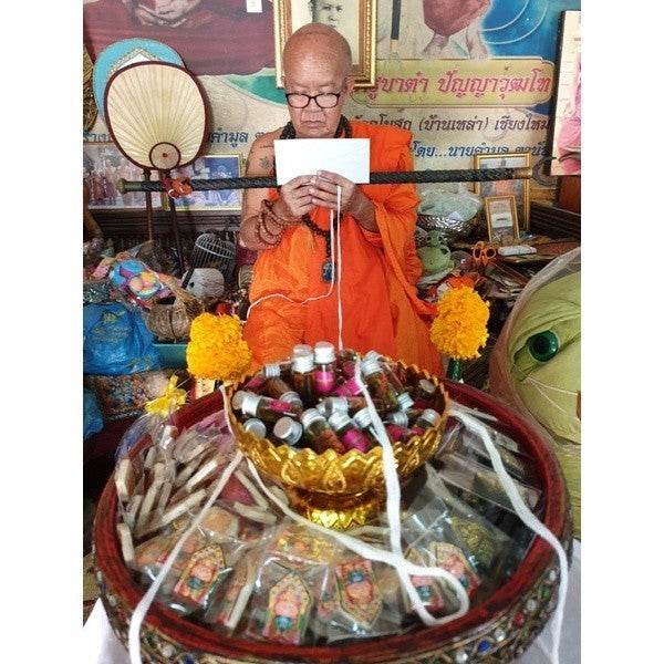 Buddhist monk preparing Thai love oil amulet at a traditional altar with offerings in a spiritual setting