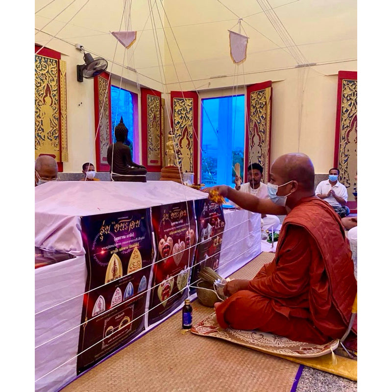 Monk performing a blessing ritual with Thai luck amulet for victory inside a decorated temple