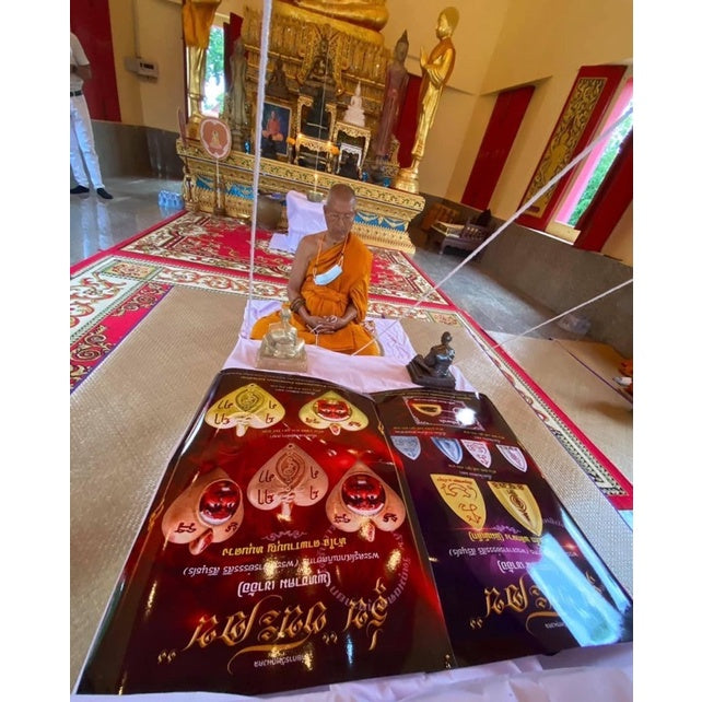 Thai monk sitting in temple with Thai luck amulet for victory displayed on red velvet cloth