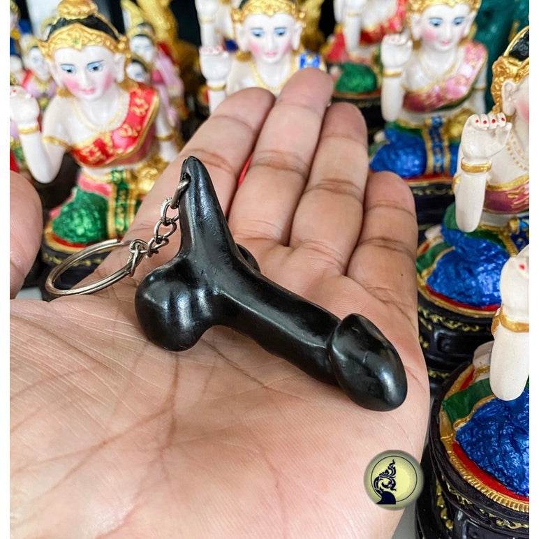 Black carved Thai lucky keychain held in palm with colorful traditional figurines background