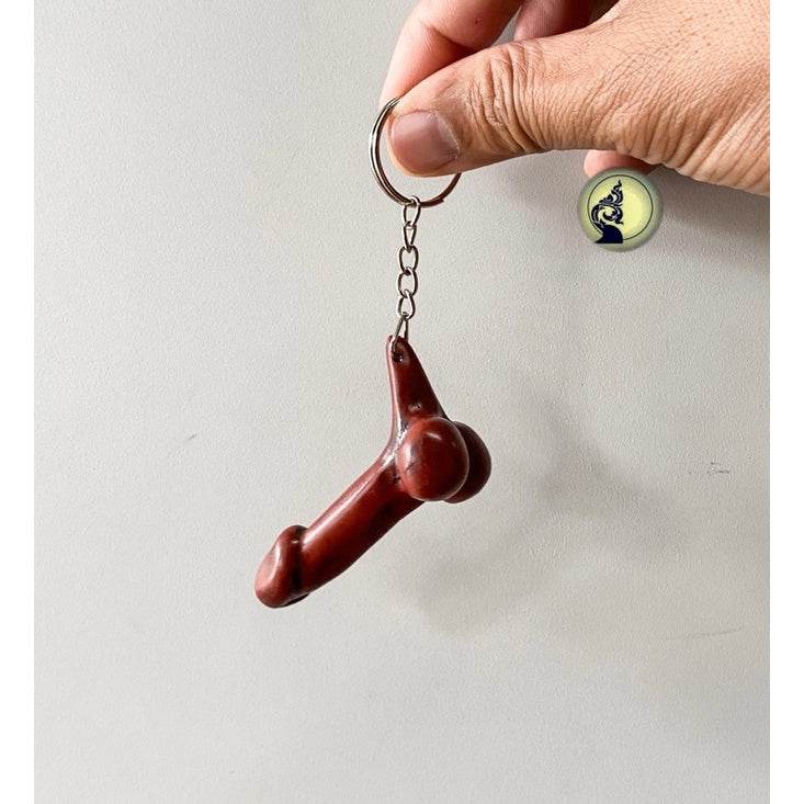 Hand holding a brown Thai lucky keychain with a unique shape and metal ring