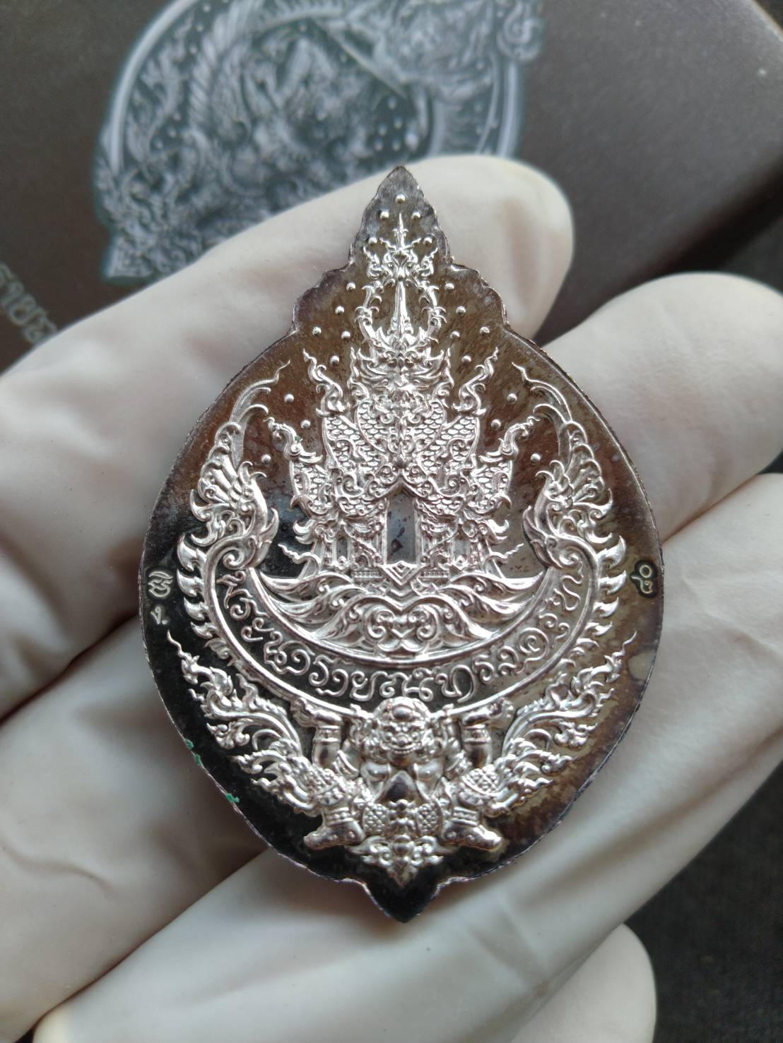 Narai on Garuda silver amulet ornate Thai devotional pendant held in white gloved hand