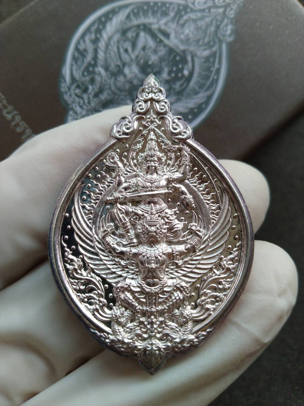 Narai on Garuda silver amulet ornate Thai pendant held in a gloved hand close up