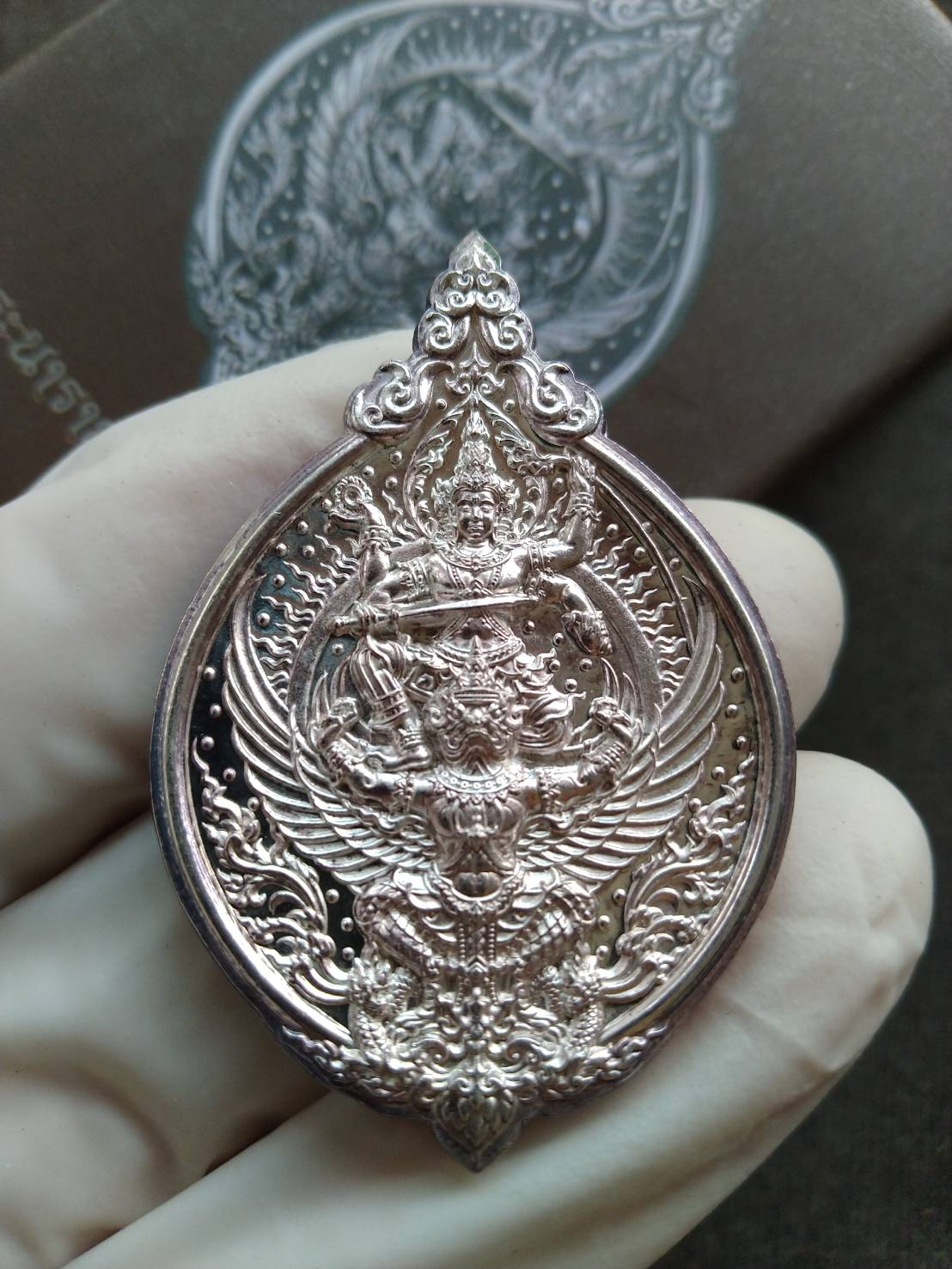 Narai on Garuda silver amulet ornate Thai pendant held in a gloved hand close up