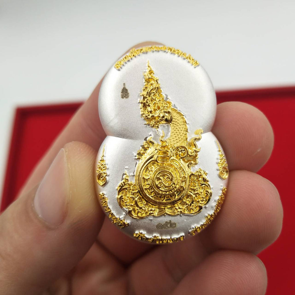 Hand holding Thai silver and gold Phra Nak Prok amulet for protection with ornate naga and sacred medallion
