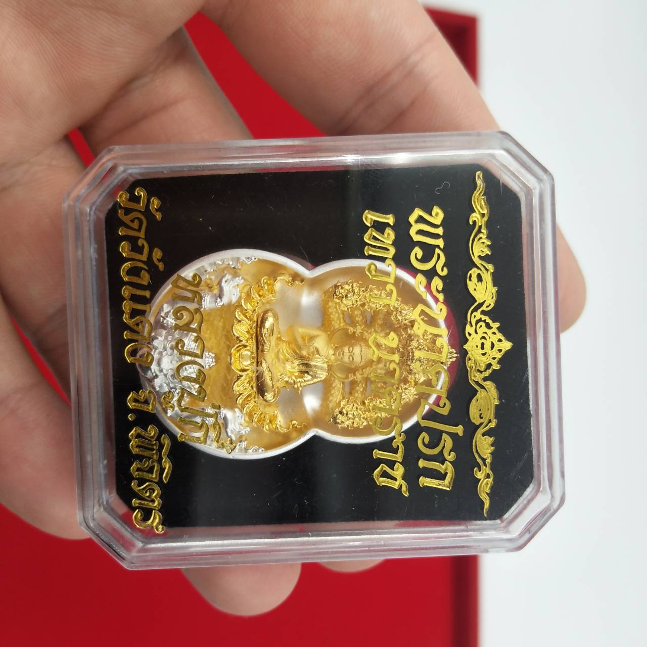 Handheld clear case with gold Phra Nak Prok amulet for protection on black backing showing Thai script