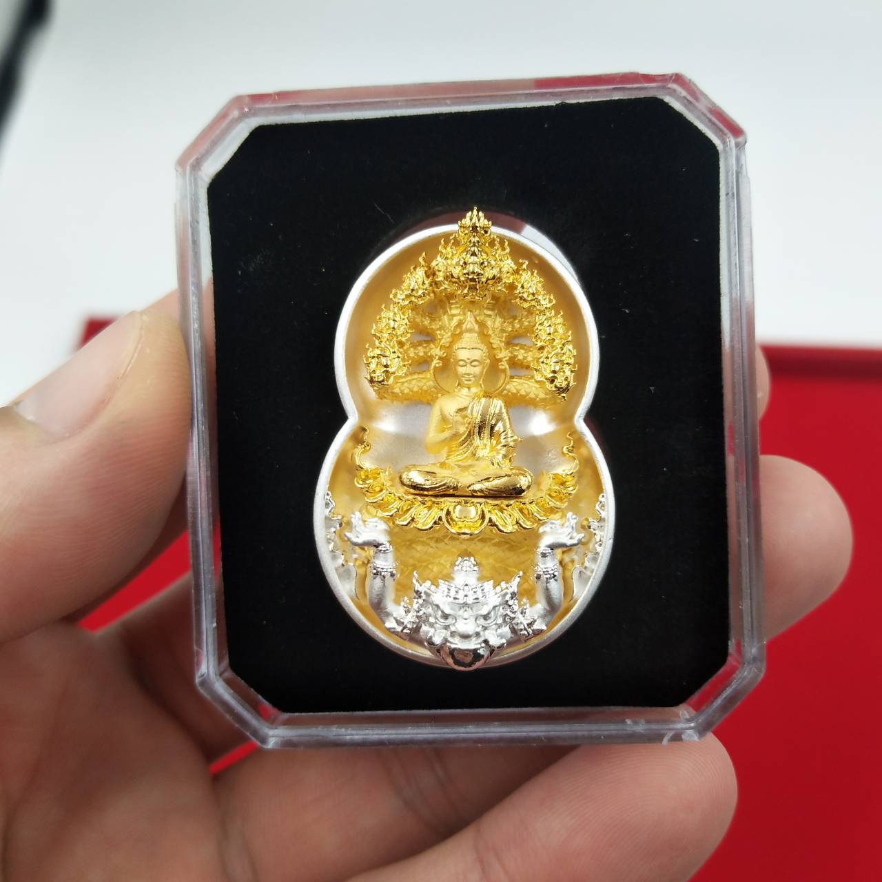 Handheld gold and silver Phra Nak Prok amulet for protection. displayed in clear case on black velvet