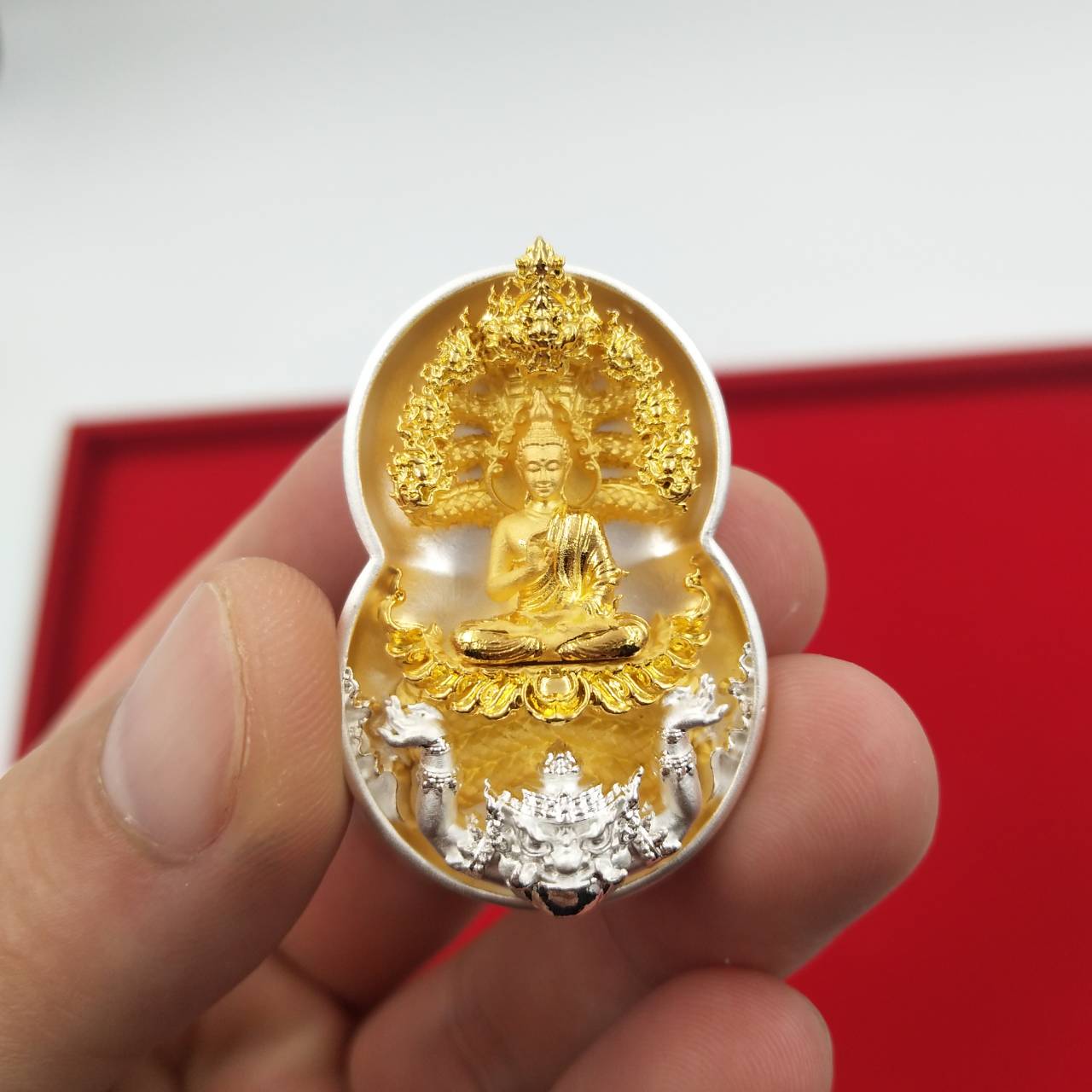 Phra Nak Prok amulet for protection. Small gold and silver amulet held between fingers showing seated Buddha under Naga canopy