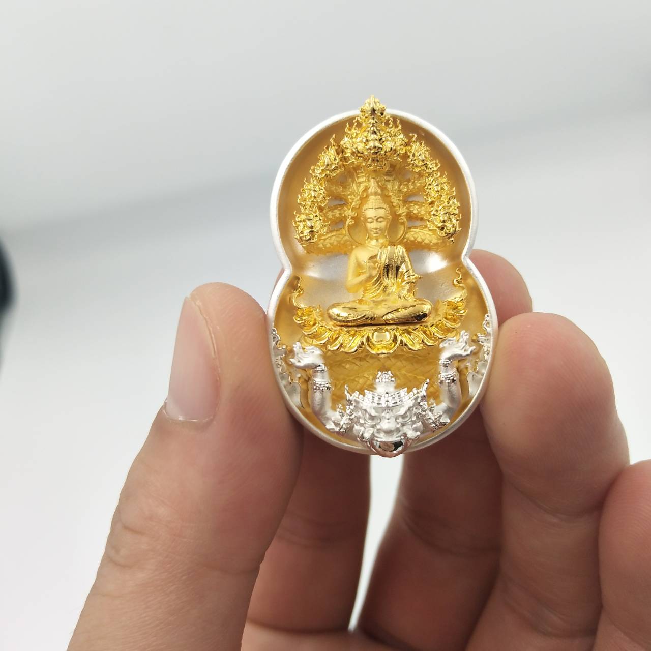Phra Nak Prok amulet for protection small gold and silver Buddha pendant held between fingers