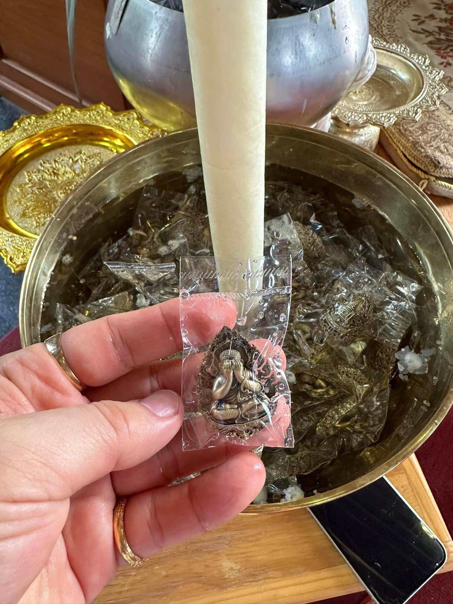 Person holding a Thai Phra Pidta amulet for protection in front of a bowl of sacred items