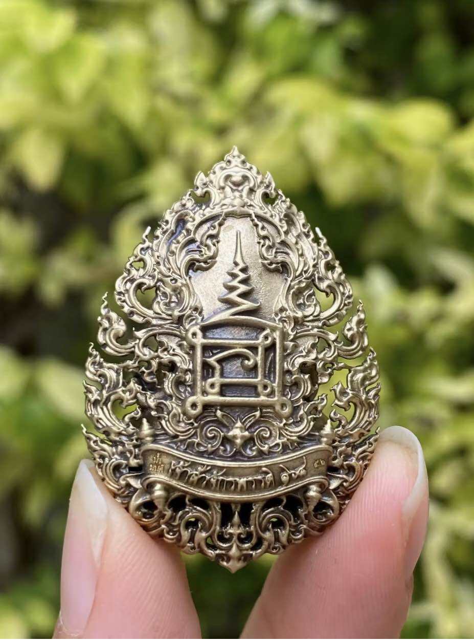Thai Phra Pidta amulet for protection intricately designed with ornate patterns, held in hand against a green background