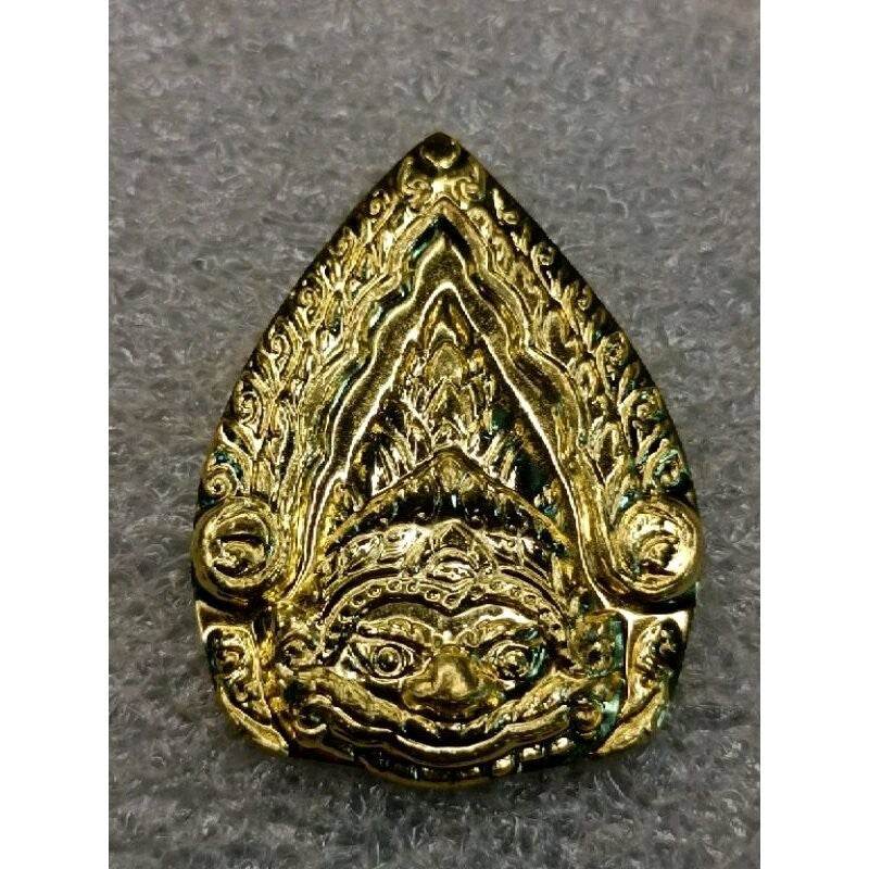 Gold Thai Phra Rahu protection amulet pendant with intricate carved Rahu face on textured gray background