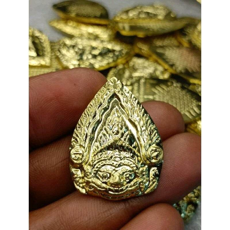 Hand holding gold engraved Phra Rahu protection amulet teardrop shaped talisman with ornate detailing