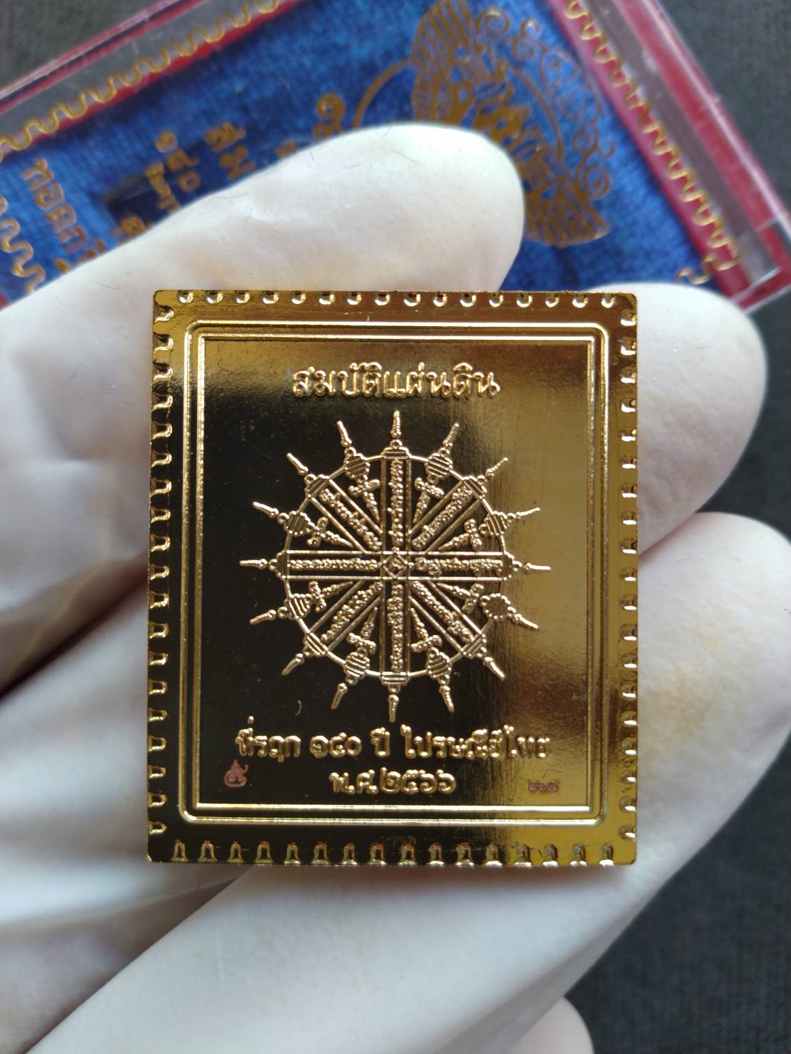 Garuda stamp medallion Thai Post gold plated rectangular amulet with intricate wheel emblem held in white glove