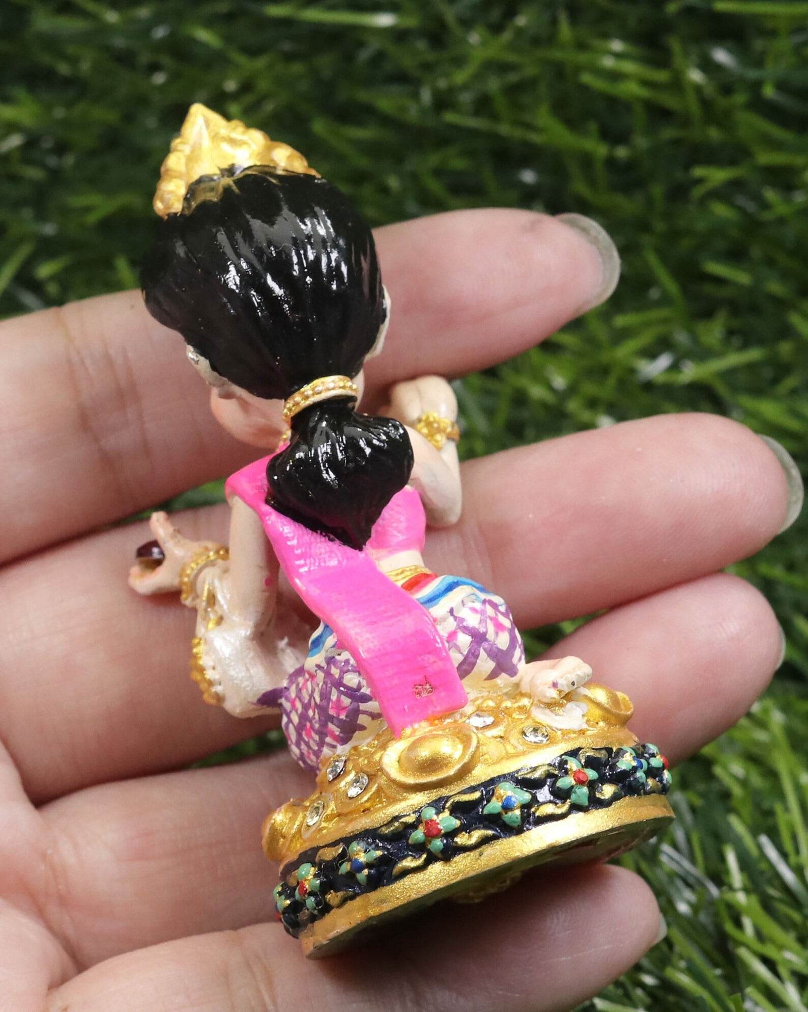 Hand holding Thai prosperity figurine for shop decor with traditional pink and gold attire