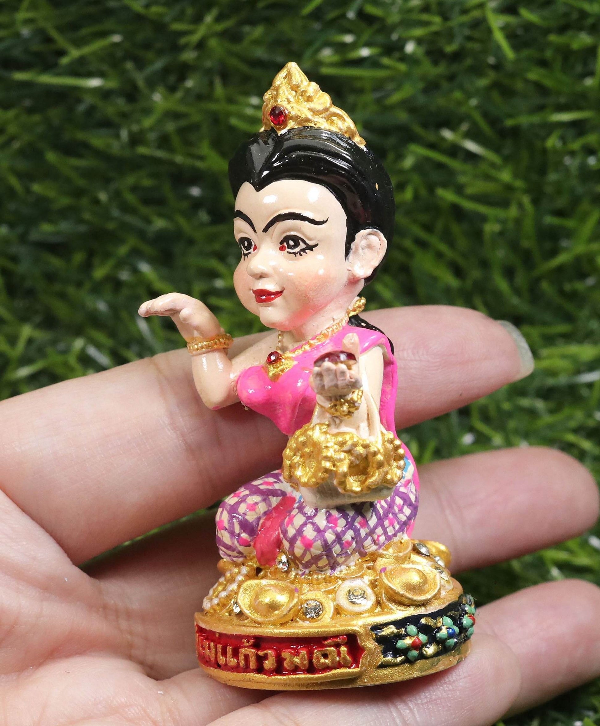 Hand holding a detailed Thai prosperity figurine for shop decor with gold and pink accents