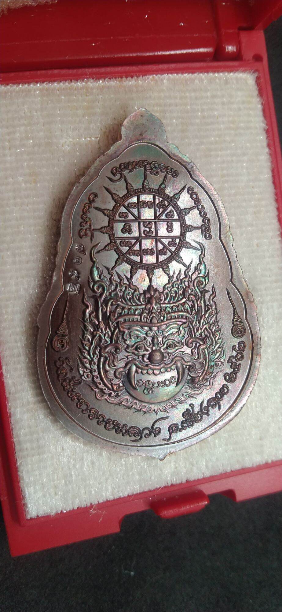 Thai protective talisman for wealth with intricate design and mythical face in red box from Thai Blessing Co
