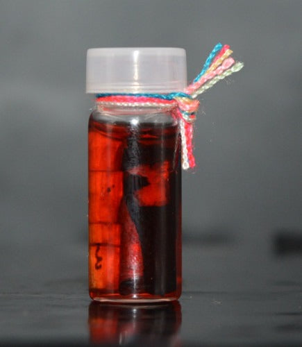 Thai Rak Yom twin child spirit amulet in a small glass bottle with red liquid and colorful string