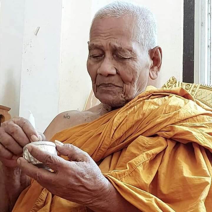 Elder Thai monk in saffron robe inspecting Ruesi Hermit Amulet Wat Khao Or for blessing