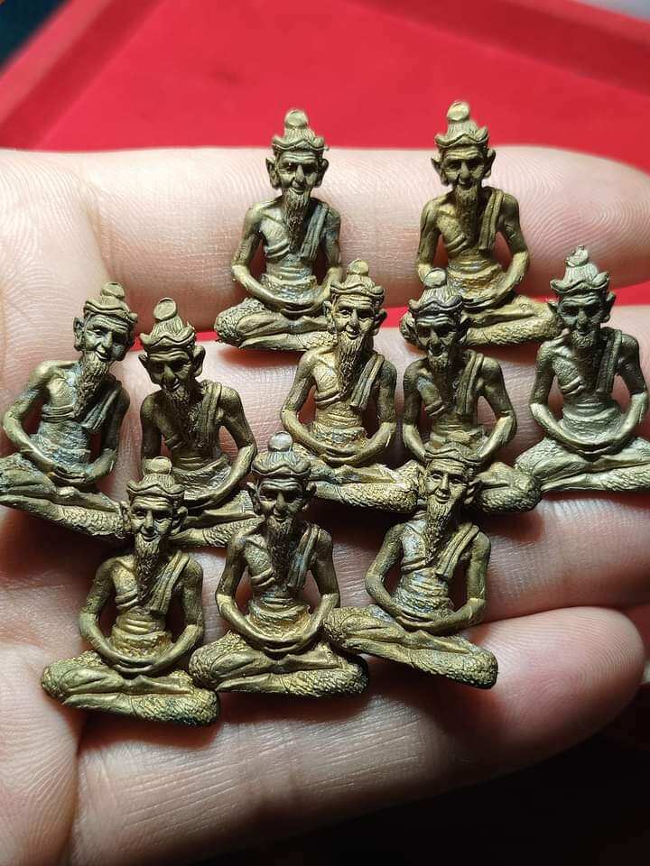 Hand holding multiple small brass hermit figurines seated cross legged Ruesi Hermit Amulet Wat Khao Or