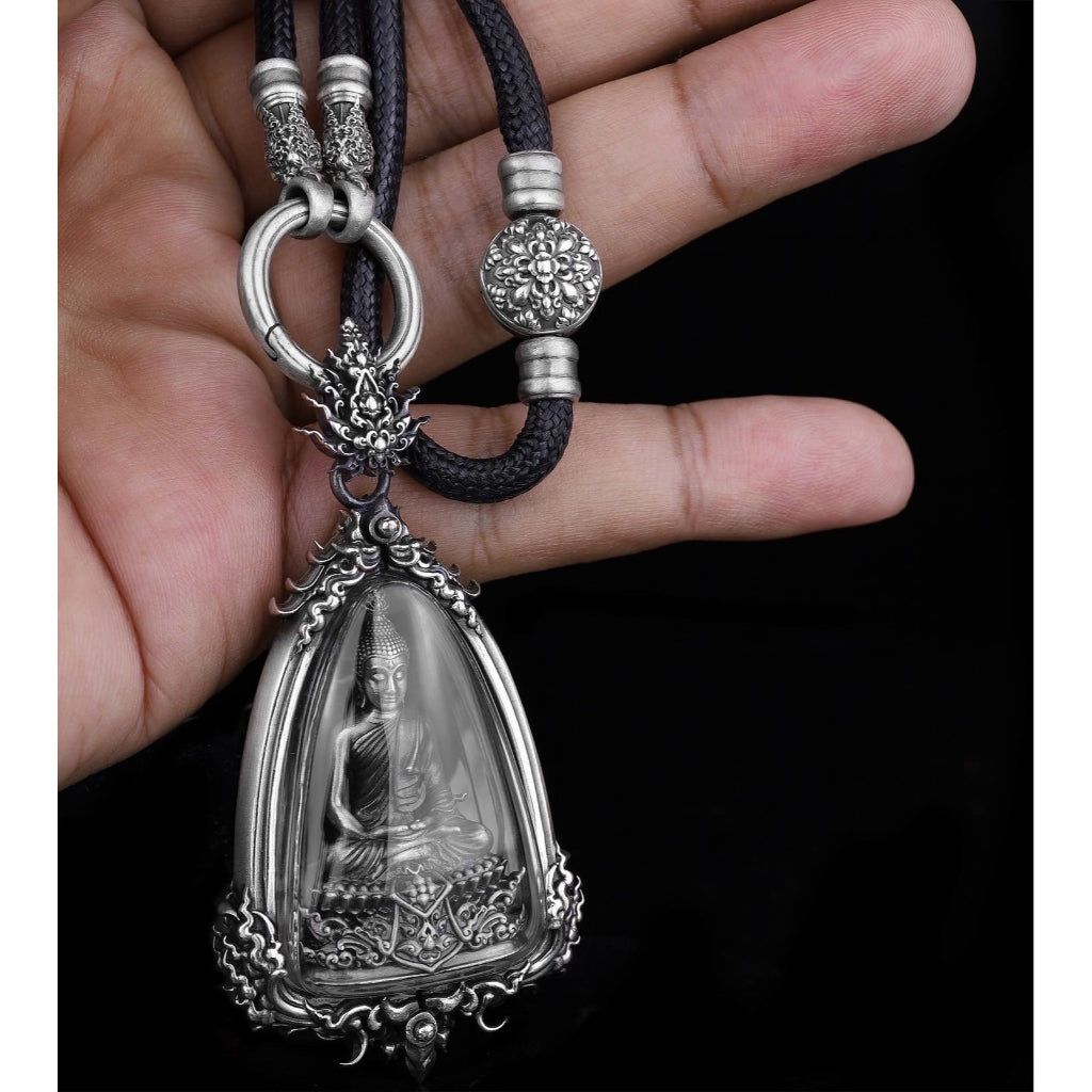 Hand holding authentic silver Buddha amulet for protection pendant with ornate Thai cord necklace