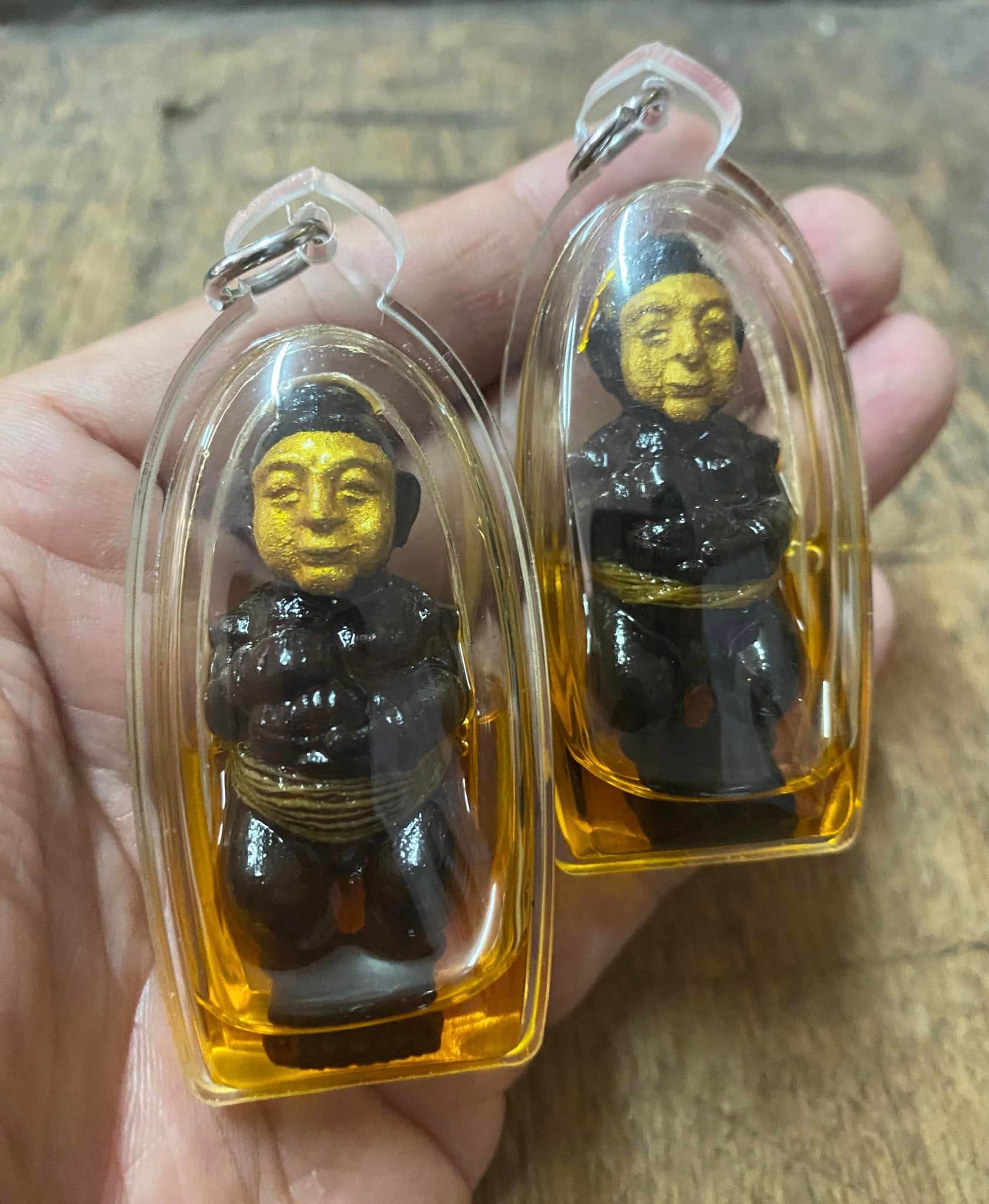 Two Thai spirit dolls for wealth and protection in clear plastic casing, perfect for good fortune.