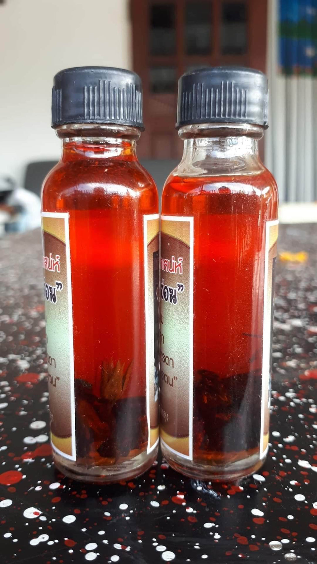 Two small bottles of Thai spiritual wealth amulet oil with black caps on a speckled surface