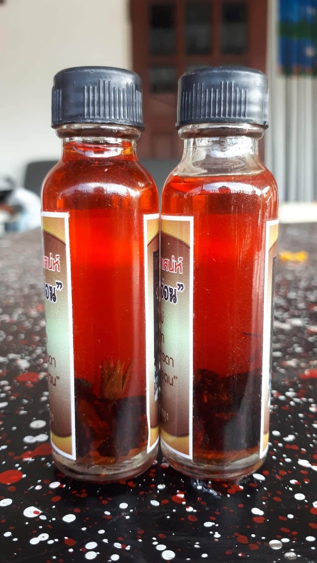 Two small bottles of Thai spiritual wealth amulet oil with black caps on a speckled surface