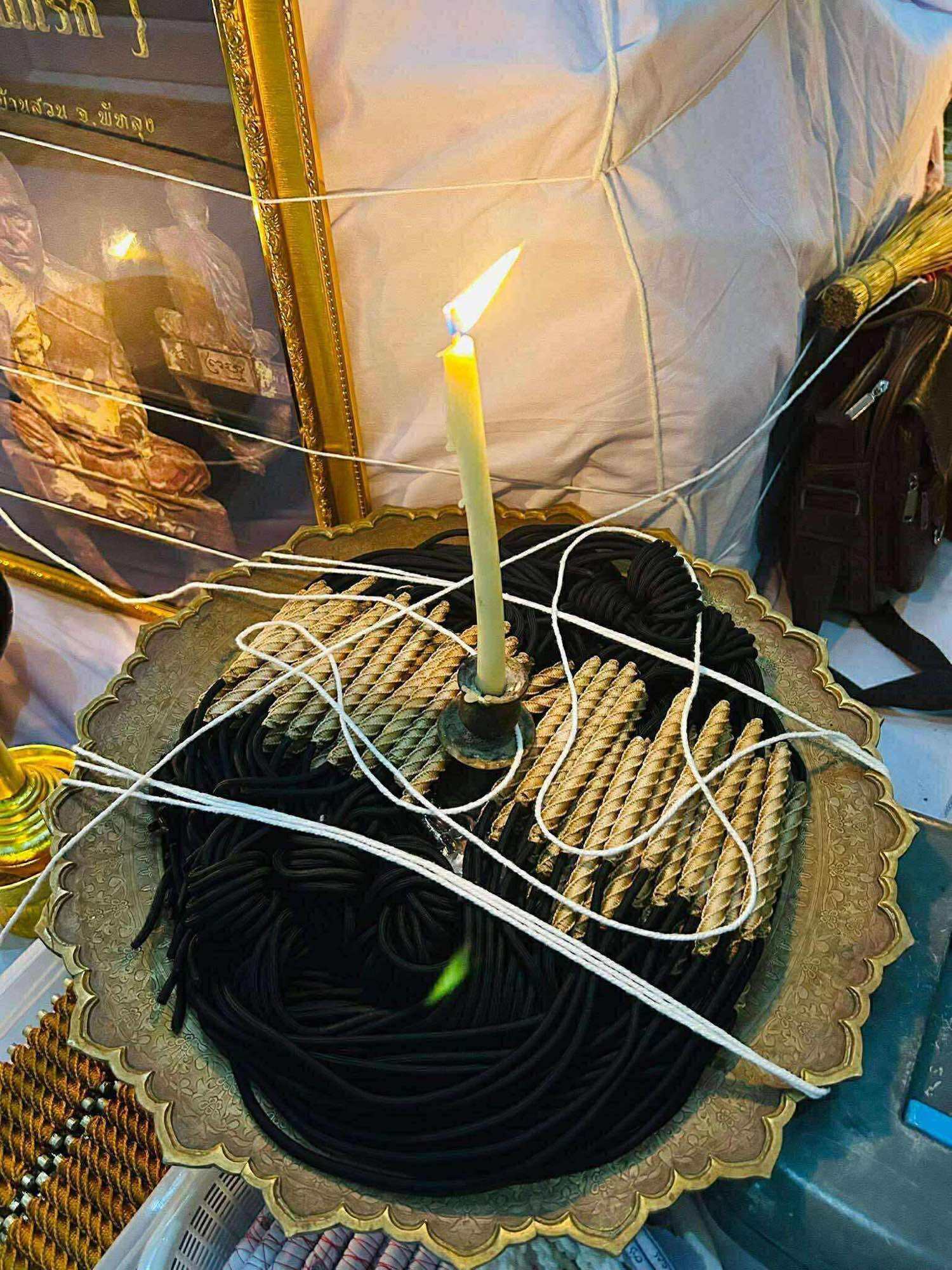 Takrud waist amulet for protection displayed on brass tray with braided cords candle and ritual strings
