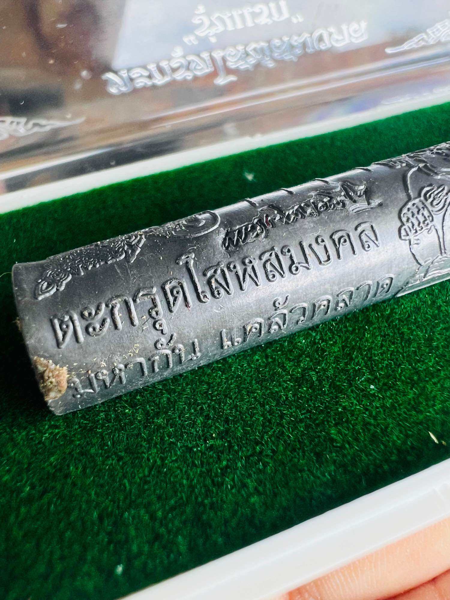 Takrut Solos Mongkol amulet metal cylinder with engraved Thai script and decorative motifs in clear display case on green felt