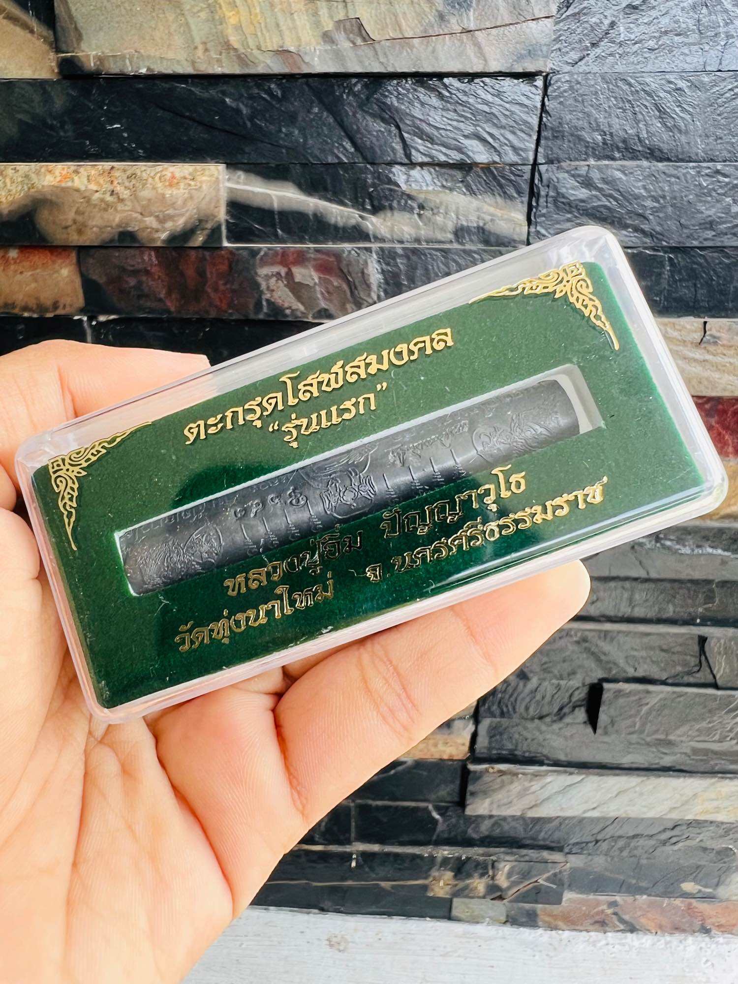 Hand holding Thai Blessing Co packaged Takrut Solos Mongkol amulet in green display box with gold Thai script