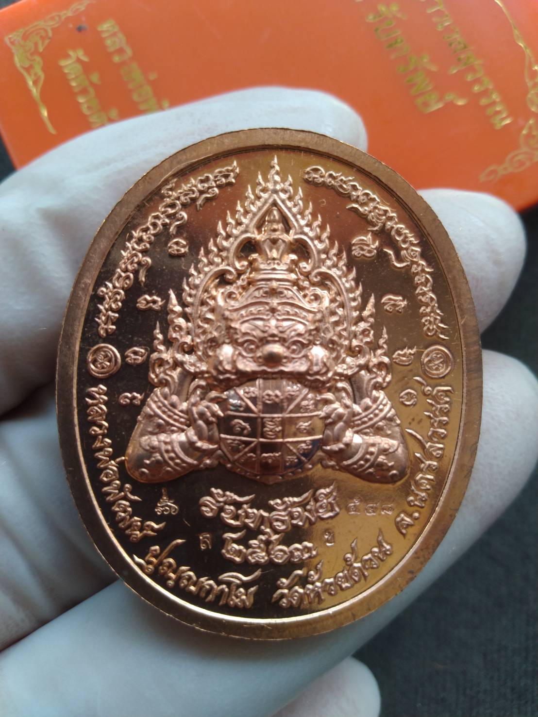 Taow Wessuwan wealth coin amulet copper medallion with embossed guardian deity and Thai script held in gloved hand