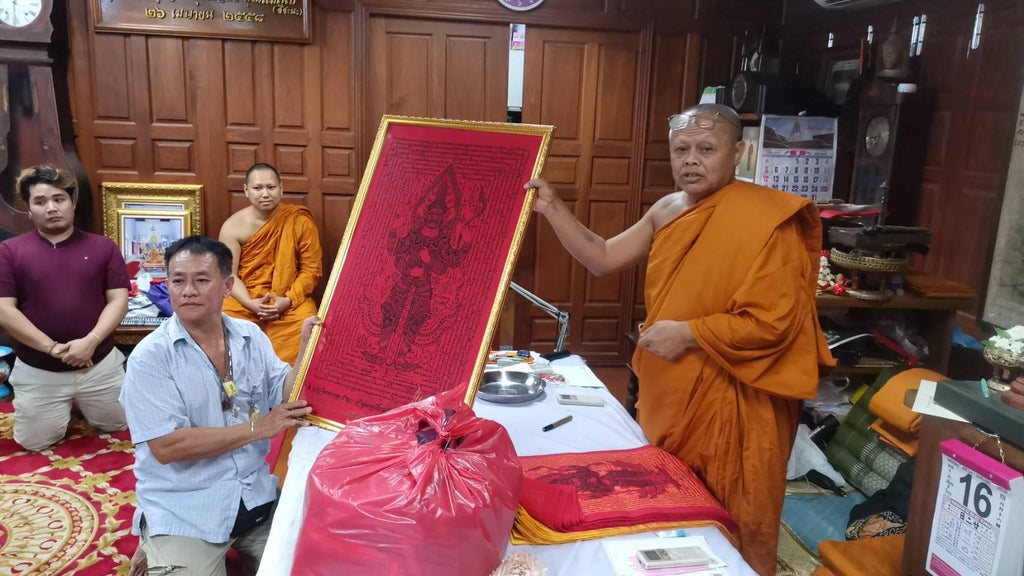 Monks and devotees in a Thai temple presenting a framed Thao Wessuwan yantra cloth red protective talisman