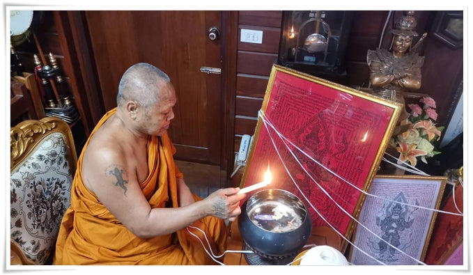 Thai monk performing a blessing ritual with framed red Thao Wessuwan yantra cloth and oil lamp