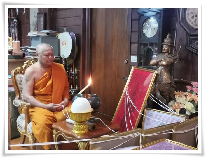 Thai monk blessing a Thao Wessuwan yantra cloth and framed talismans in a traditional ritual setting