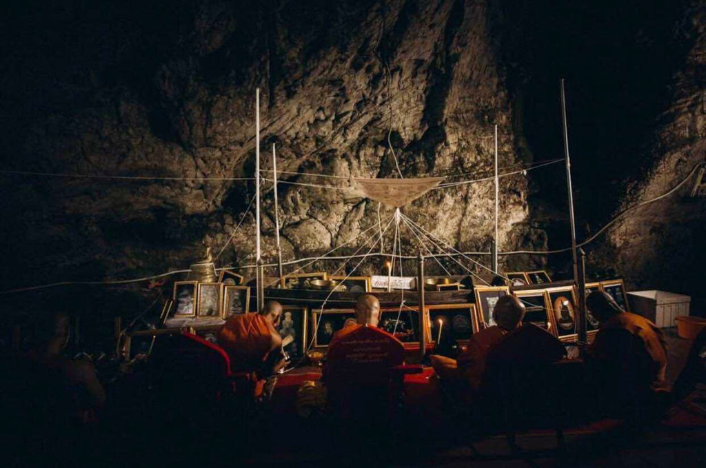 Thai tiger amulet for protection displayed in a dimly lit cave with monks praying nearby
