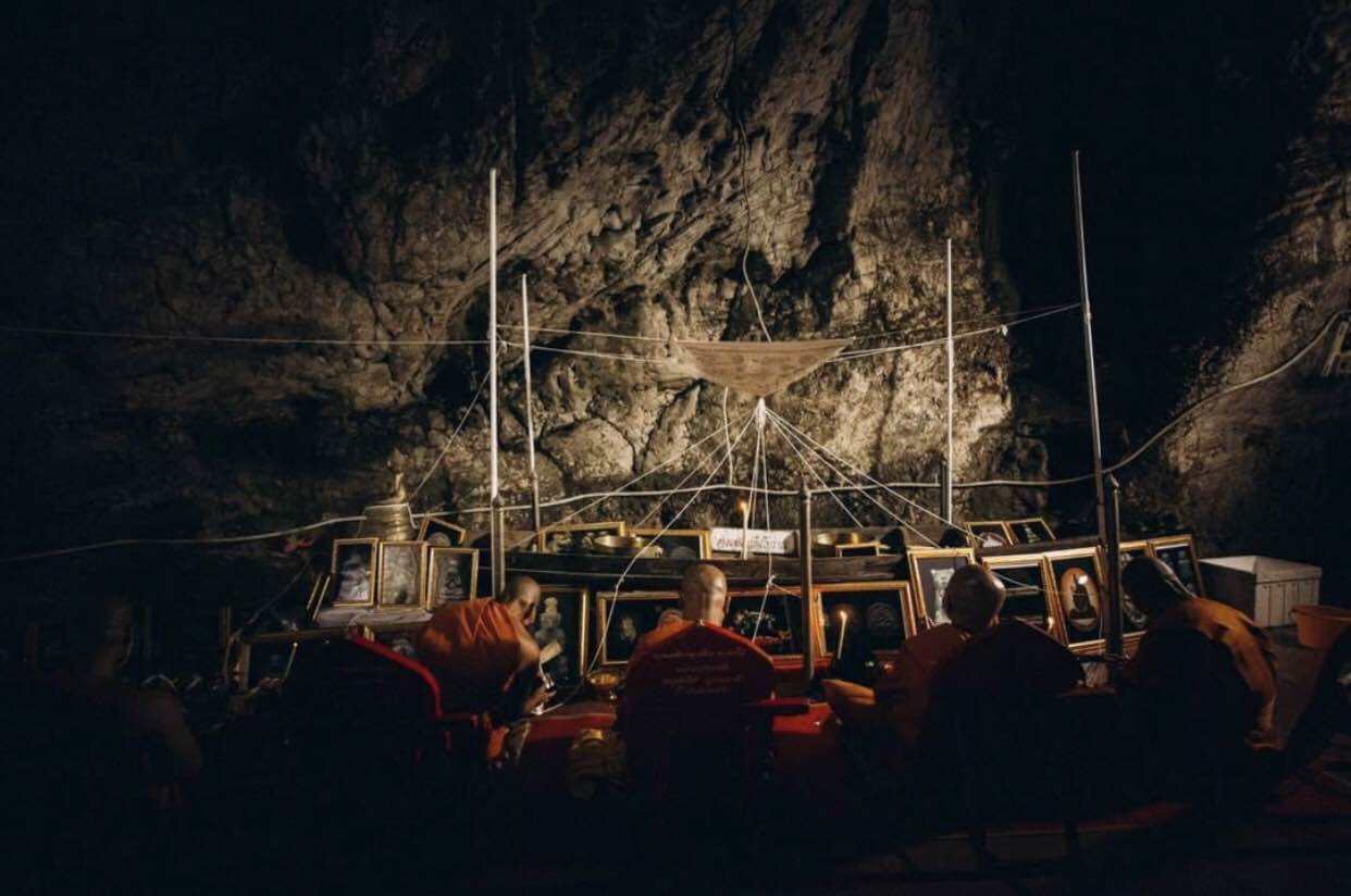 Thai tiger amulet for protection displayed in a dimly lit cave with monks praying nearby
