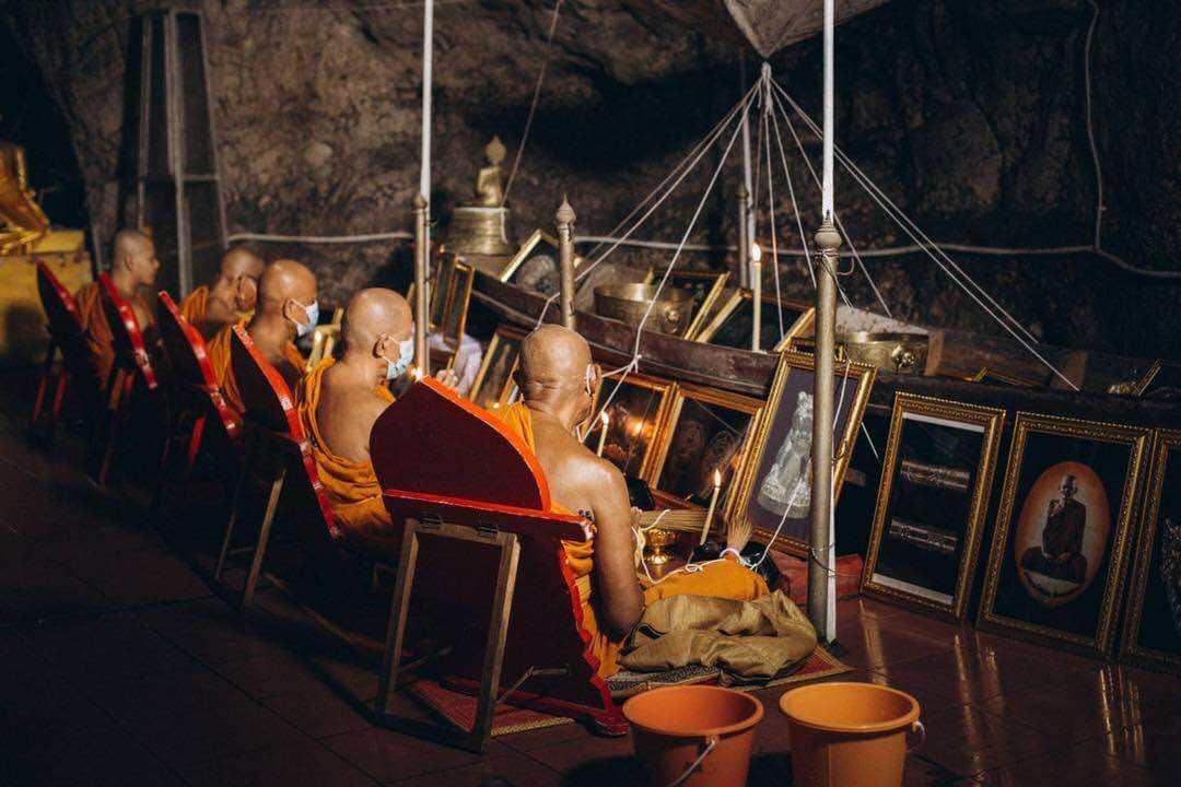 Monks praying in a dimly lit cave surrounded by framed images and Buddhist ornaments