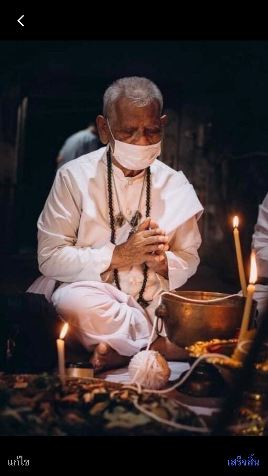 Elderly man in white traditional attire praying with candles and offerings, symbolizing Thai tiger amulet for protection