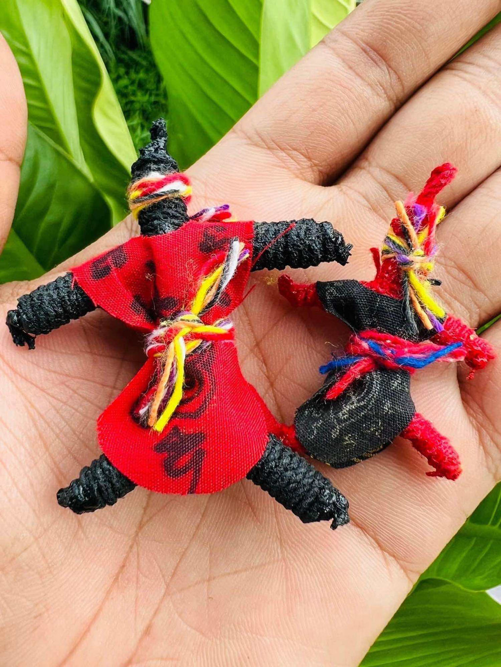Hoon Payon amulet dolls Thailand two small black string spirit dolls wrapped in red cloth with colorful thread ties held in palm