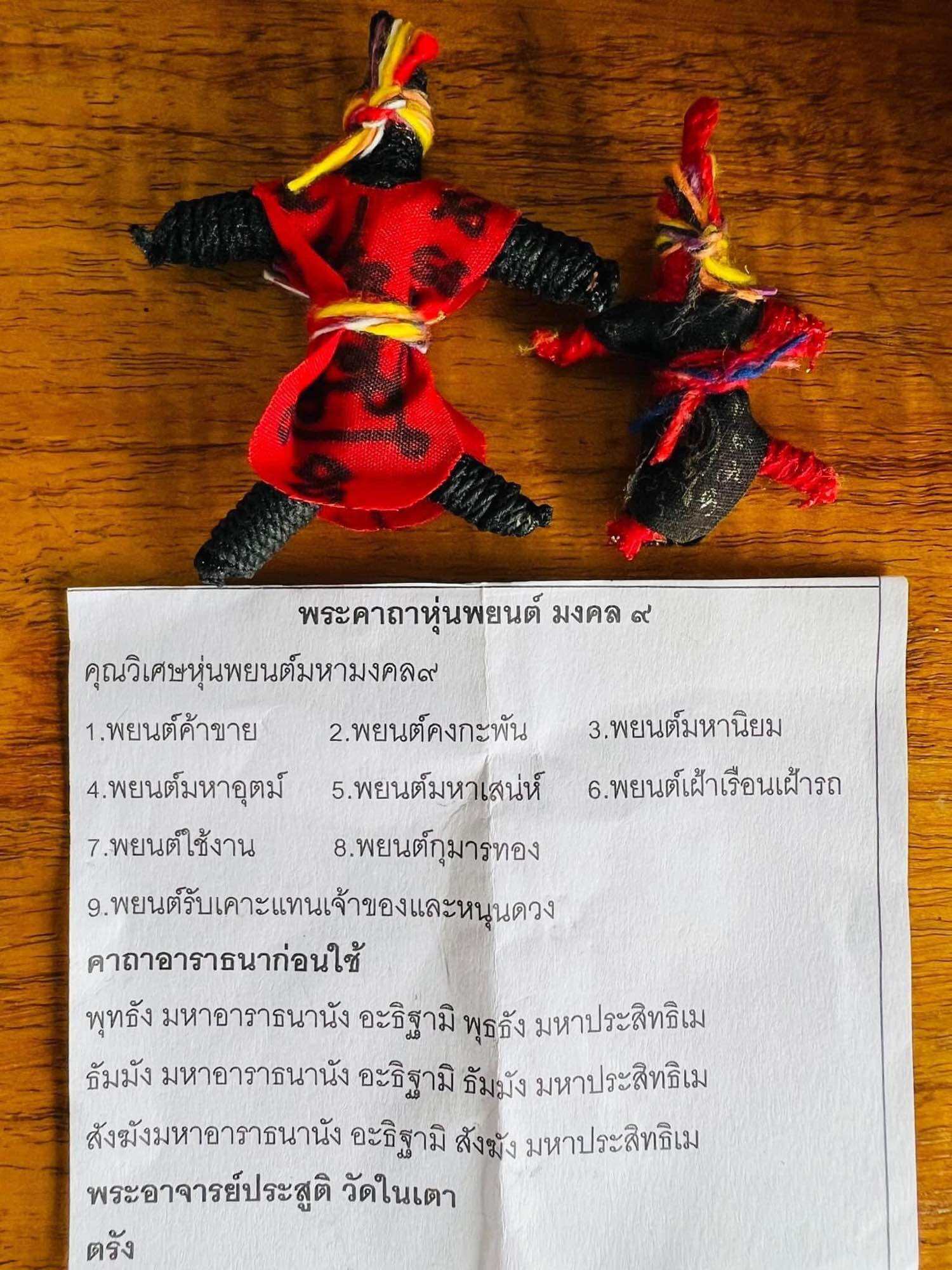 Hoon Payon amulet dolls Thailand two handmade black and red cloth spirit dolls on a wooden table with Thai blessing paper