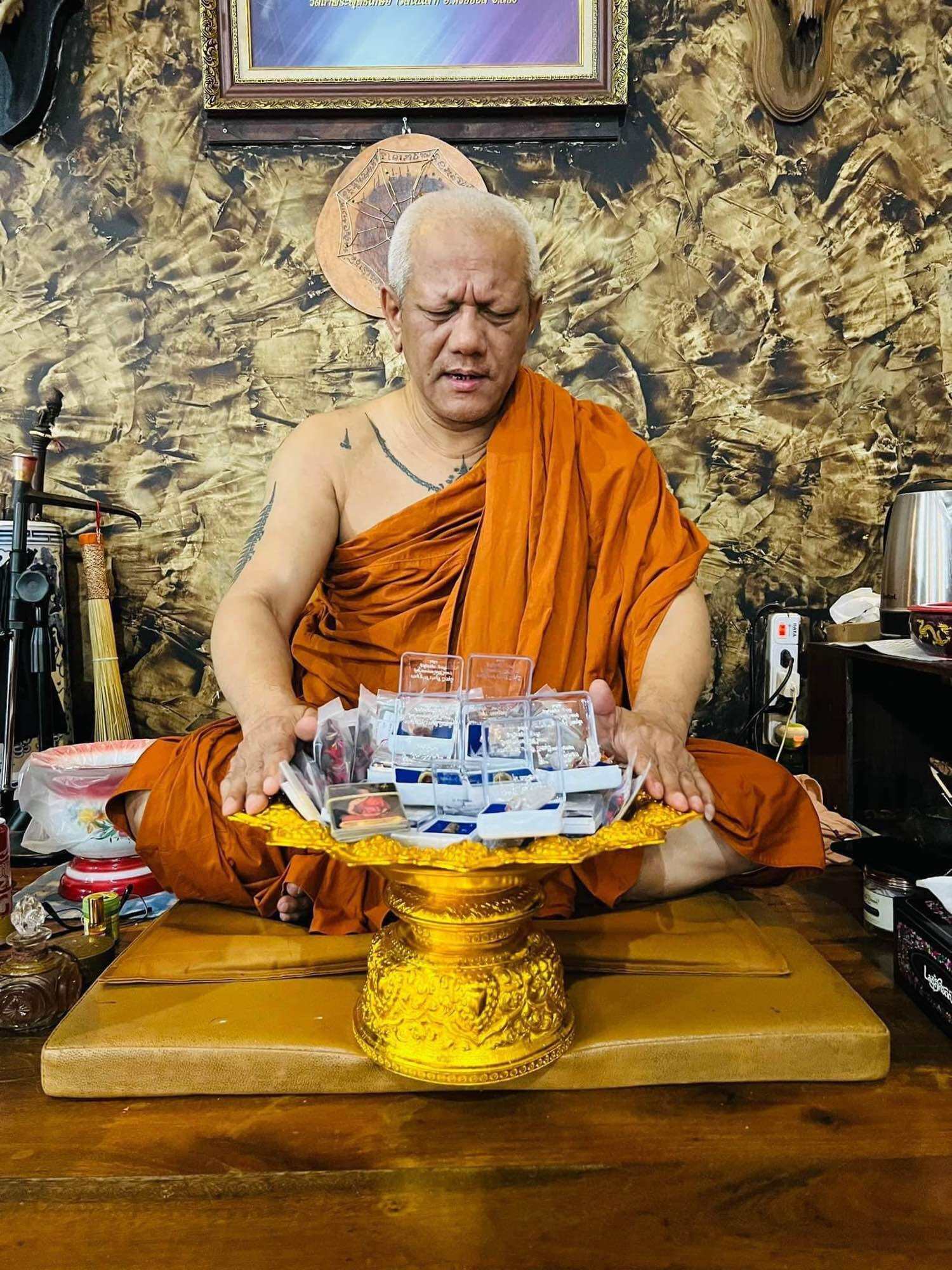 Thai monk blessing Hoon Payon amulet dolls Thailand on golden tray in temple setting for consecration