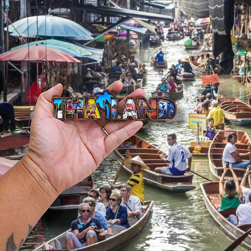 Hand holding a colorful thai wood magnet souvenir with Thailand letters at a floating market
