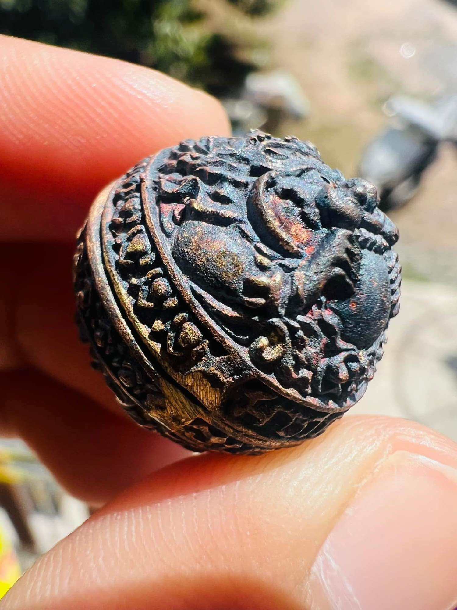 Small ornate round metal amulet with lion motif and dark patina held between fingers ancient Thai talisman first edition