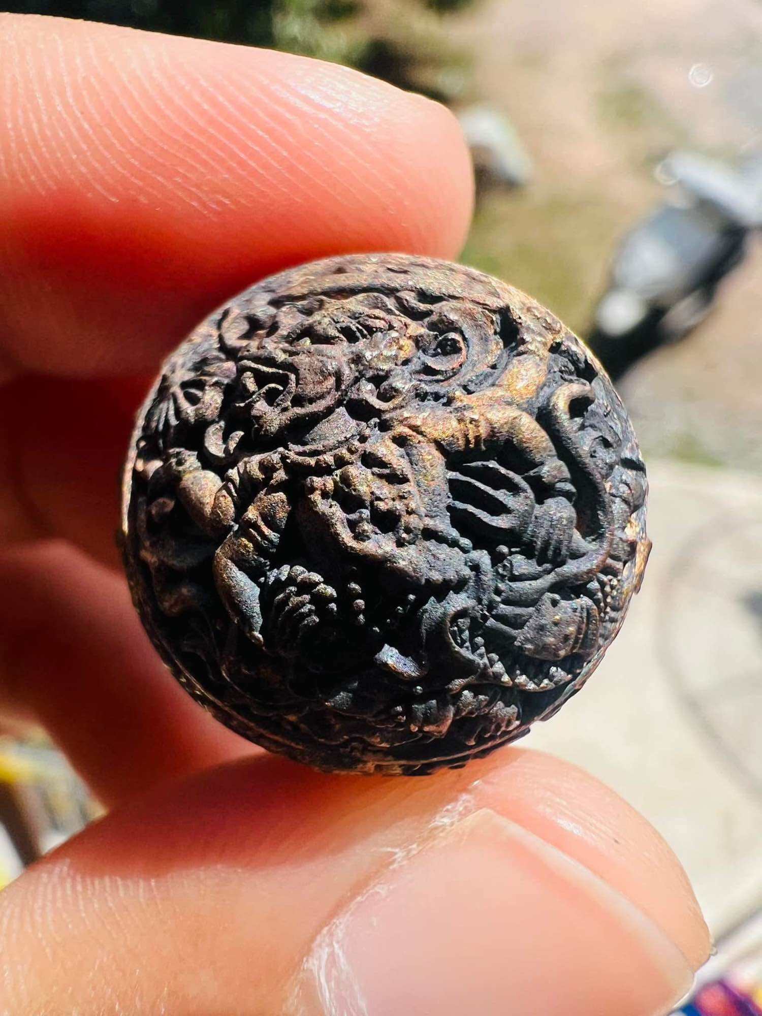 Close up of weathered carved round pendant held between fingers ancient Thai talisman first edition