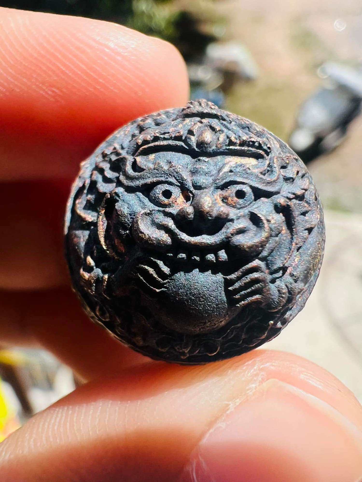 Handheld aged metal amulet pendant with guardian face details ancient Thai talisman first edition from Thai Blessing Co