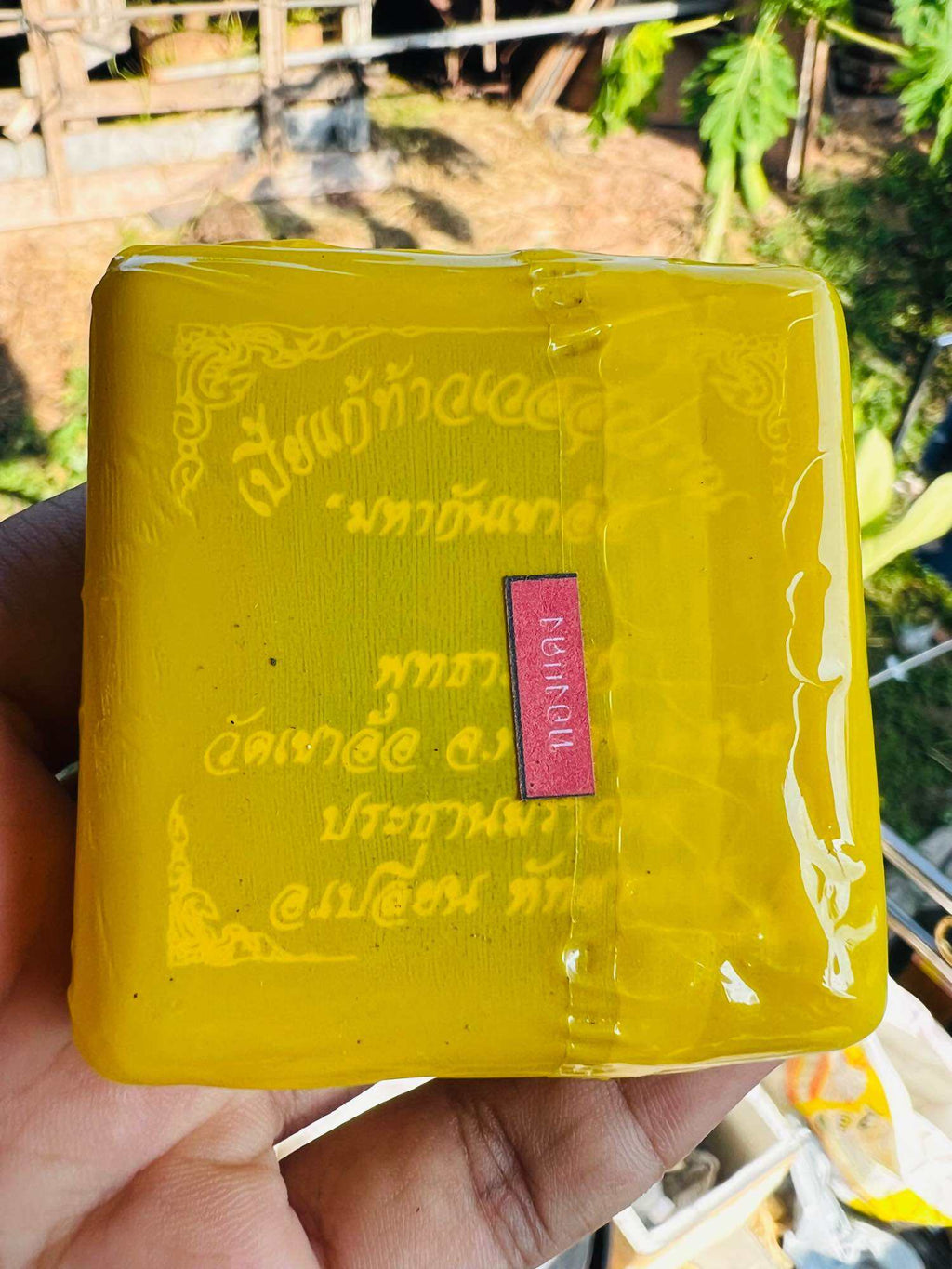 Bia Gae amulet for protection wrapped in yellow packaging with red label held in hand Thai Blessing Co