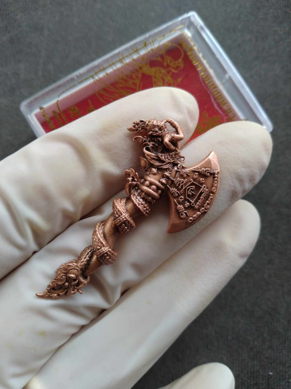 Copper carved pendant held in gloved hand featuring serpent and deity motifs blessed Thai Sky Axe for luck